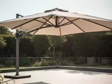 Ein hochwertiger, heller Sonnenschirm spendet Schatten auf einer sonnigen Terrasse, symbolisiert UV-Schutz und Stabilität. - Foto: über boerse-global.de