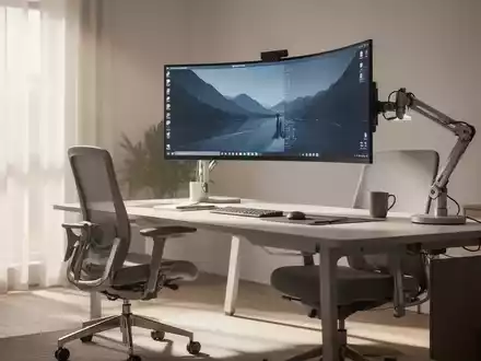 Ein modernes Homeoffice mit ergonomischem Schreibtischstuhl, höhenverstellbarem Schreibtisch und einem großen gebogenen Monitor an einem Monitorarm. - Foto: über boerse-global.de