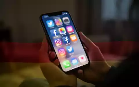 Eine junge Person hält ein Smartphone mit verschwommenen Social-Media-Symbolen auf dem Bildschirm, überlagert von den deutschen Farben. - Foto: über boerse-global.de