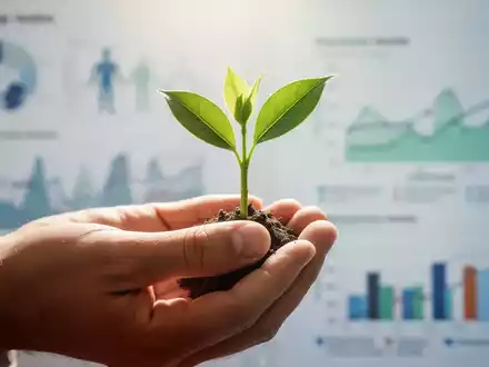 Eine Hand hält eine kleine, sprießende Pflanze, die Gesundheit und Wachstum symbolisiert, mit verschwommenen medizinischen Diagrammen im Hintergrund. - Foto: über boerse-global.de