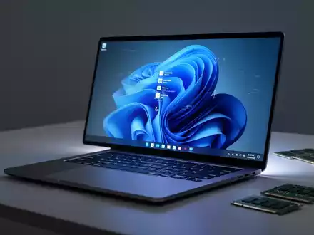 A modern laptop with a Windows 11 screen sits on a desk, next to out-of-focus RAM sticks, symbolizing computing and hardware. - Foto: über boerse-global.de