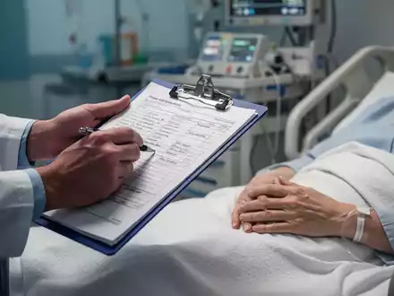 Nahaufnahme der Hände eines medizinischen Fachpersonals, das ein Klemmbrett mit Notizen hält, und der Hand eines Patienten auf einem Krankenhausbett. - Foto: über boerse-global.de