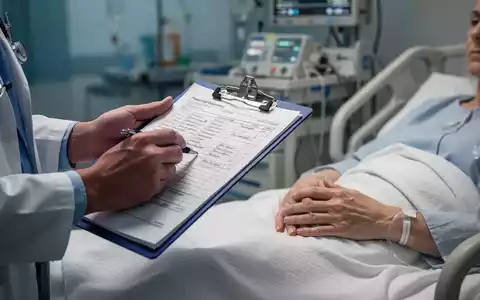 Nahaufnahme der Hände eines medizinischen Fachpersonals, das ein Klemmbrett mit Notizen hält, und der Hand eines Patienten auf einem Krankenhausbett. - Foto: über boerse-global.de