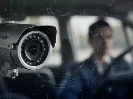 Eine Nahaufnahme einer Überwachungskamera mit digitalem Overlay, die auf die Silhouette einer Person in einem Fahrzeug gerichtet ist. - Foto: über boerse-global.de