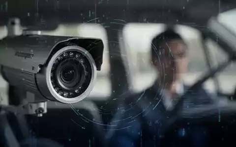 Eine Nahaufnahme einer Überwachungskamera mit digitalem Overlay, die auf die Silhouette einer Person in einem Fahrzeug gerichtet ist. - Foto: über boerse-global.de