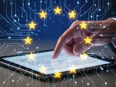 Eine stilisierte, leuchtende neuronale Netzwerkschaltung mit EU-Sternen und einer Hand, die eine Tablet mit Gesetzestext berührt. - Foto: über boerse-global.de