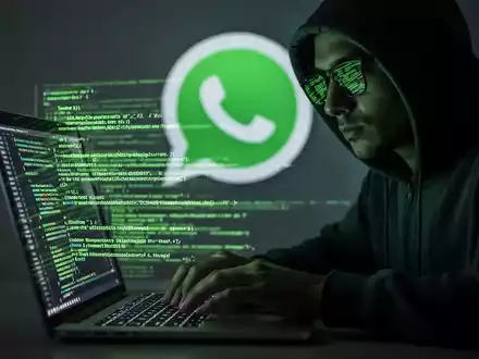 Verschwommene Gestalt in Kapuzenjacke tippt auf Laptop mit grün leuchtendem Code, symbolisiert Cyberangriff auf WhatsApp-Nutzer. - Foto: über boerse-global.de