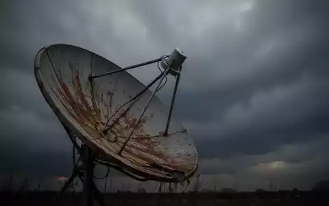 Eine leicht verrostete Satellitenschüssel zeigt in einen dunklen, bewölkten Himmel, der einen Rückgang symbolisiert. - Foto: über boerse-global.de