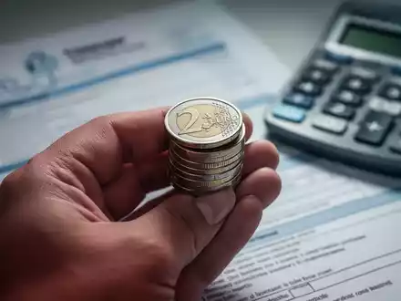 Eine Hand hält einen Stapel Euromünzen, im unscharfen Hintergrund sind medizinische Dokumente und ein Taschenrechner zu sehen. - Foto: über boerse-global.de