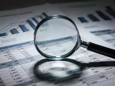 Eine Nahaufnahme eines Vergrößerungsglases über einem Finanzbericht, mit unscharfen Diagrammen und Grafiken im Hintergrund. - Foto: über boerse-global.de