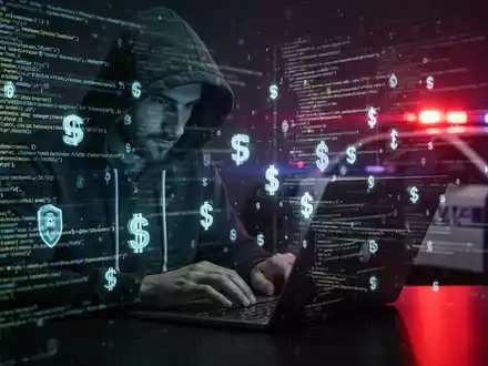 Person in Kapuzenjacke tippt auf Laptop, umgeben von Codezeilen und Kryptowährungssymbolen, mit Reflexion von Polizeilichtern. - Foto: über boerse-global.de