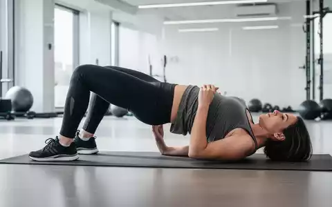 Eine Person führt eine Hüftbrücke auf einer Yogamatte in einem modernen Fitnessstudio aus, Fokus auf die Hüftregion. - Foto: über boerse-global.de