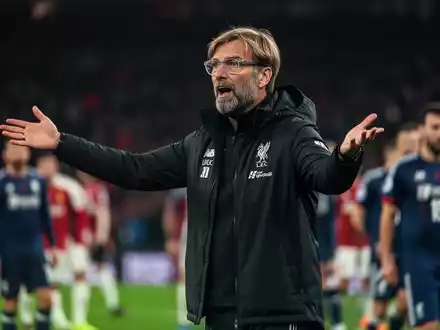 Jürgen Klopp gestikuliert am Spielfeldrand, im Hintergrund ein unscharfes Fußballstadion und Spieler. - Foto: über boerse-global.de