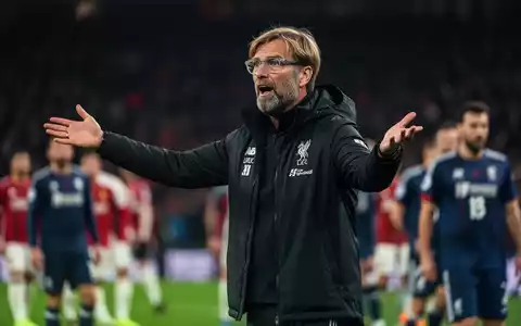 Jürgen Klopp gestikuliert am Spielfeldrand, im Hintergrund ein unscharfes Fußballstadion und Spieler. - Foto: über boerse-global.de