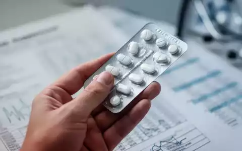 Eine Hand hält eine Blisterpackung mit Pillen, im unscharfen Hintergrund sind medizinische Diagramme zu sehen. - Foto: über boerse-global.de