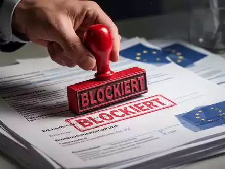 Eine Nahaufnahme einer Hand, die einen roten Stempel mit der Aufschrift „BLOCKIERT“ auf Dokumente zu EU-Richtlinien und Arbeitsgesetzen drückt. - Foto: über boerse-global.de