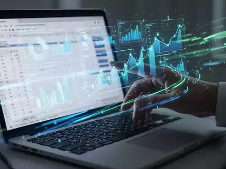 Eine Hand interagiert mit einer holografischen Projektion von Finanzdatenvisualisierungen über einem Laptop mit einer Excel-Tabelle. - Foto: über boerse-global.de