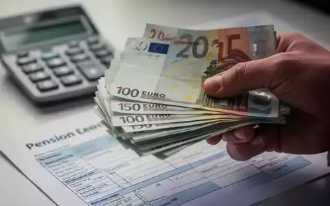 Eine Nahaufnahme einer Hand, die Euro-Banknoten hält, mit einem unscharfen Taschenrechner und einem Rentenbescheid im Hintergrund. - Foto: über boerse-global.de