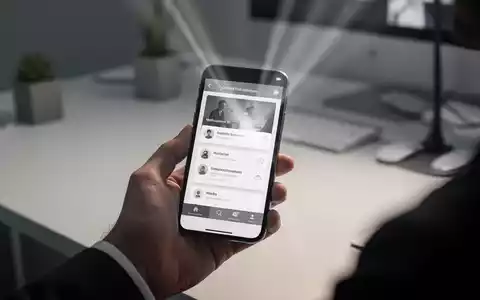 Handy mit Graustufen-Bildschirm in der Hand, unscharfer Schreibtisch im Hintergrund. - Foto: über boerse-global.de