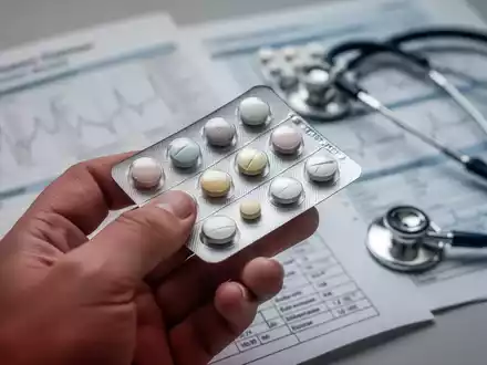 Eine Hand hält eine Blisterpackung mit Pillen, im Hintergrund verschwommene medizinische Diagramme und ein Stethoskop. - Foto: über boerse-global.de