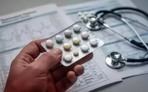 Eine Hand hält eine Blisterpackung mit Pillen, im Hintergrund verschwommene medizinische Diagramme und ein Stethoskop. - Foto: über boerse-global.de