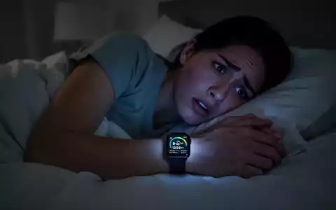 Eine Person liegt wach und ängstlich im Bett, beleuchtet vom Display einer Smartwatch, die Schlafdaten anzeigt. - Foto: über boerse-global.de