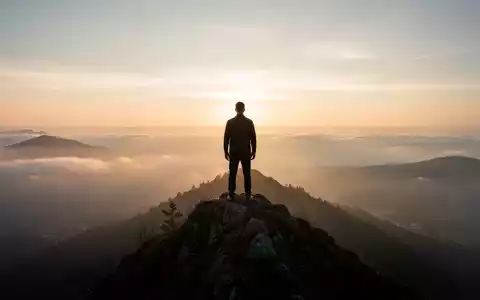 Eine Silhouette steht auf einem Berggipfel bei Sonnenaufgang und blickt auf eine weite, neblige Landschaft, die mentale Resilienz symbolisiert. - Foto: über boerse-global.de
