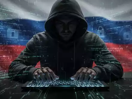 Verschattete Gestalt in Kapuzenjacke tippt auf leuchtender Tastatur, umgeben von digitalem Code, symbolisiert russische Cyber-Spionage. - Foto: über boerse-global.de