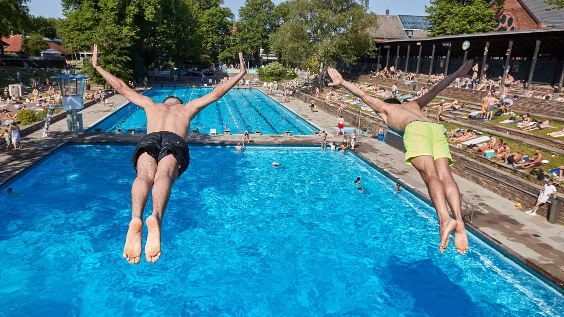 Zwei Männer springen vom Fünf-Meter-Turm in das Becken im Sommerfreibad Kaifu-Bad in Hamburg. - Bild: Georg Wendt/dpa