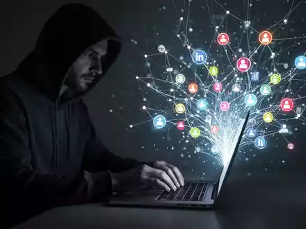 Eine schattenhafte Gestalt in Kapuzenpulli tippt auf Laptop, umgeben von leuchtendem digitalem Netzwerk und Social-Media-Symbolen. - Foto: über boerse-global.de