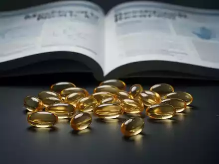 Omega-3-Fischölkapseln liegen auf einer dunklen Oberfläche, im Hintergrund eine unscharfe medizinische Forschungszeitschrift. - Foto: über boerse-global.de