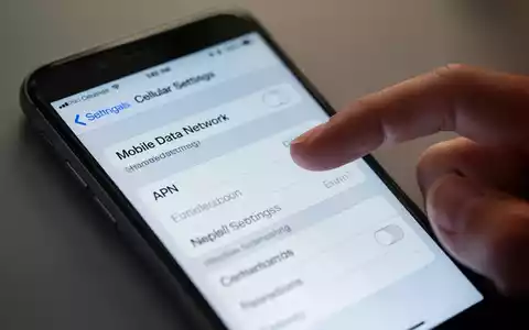 Nahaufnahme eines iPhone-Bildschirms mit Mobilfunkeinstellungen, Finger kurz vor dem Tippen. Anzeige von 'Mobiles Datennetz' und APN-Feldern. - Foto: über boerse-global.de