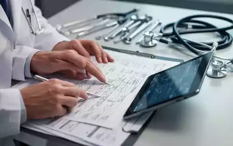 Nahaufnahme der Hände eines Arztes, der medizinische Unterlagen und ein Tablet prüft, mit verschwommenen Instrumenten im Hintergrund. - Foto: über boerse-global.de