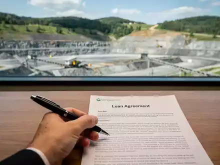 Eine Hand hält einen Stift über einem Kreditvertrag, im Hintergrund eine nachhaltige Graphitmine. - Foto: über boerse-global.de