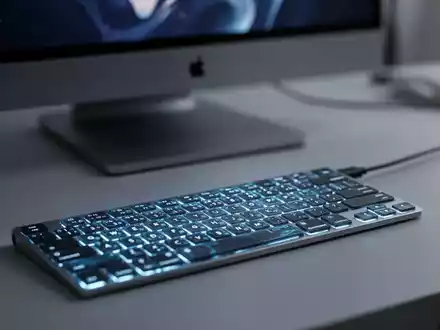 Moderne, hintergrundbeleuchtete Tastatur auf einem Schreibtisch vor einem verschwommenen Apple MacBook, das Mac-Peripherietechnologie zeigt. - Foto: über boerse-global.de