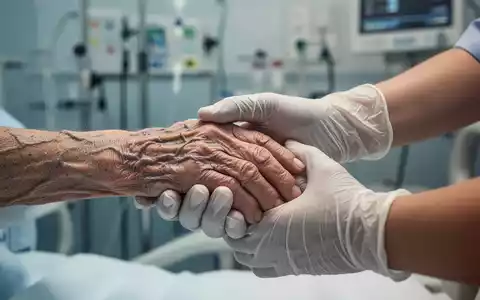 Eine ältere Hand wird von einer jüngeren, behandschuhten Hand in einer Notaufnahme gehalten, die Fürsorge und Verletzlichkeit symbolisiert. - Foto: über boerse-global.de