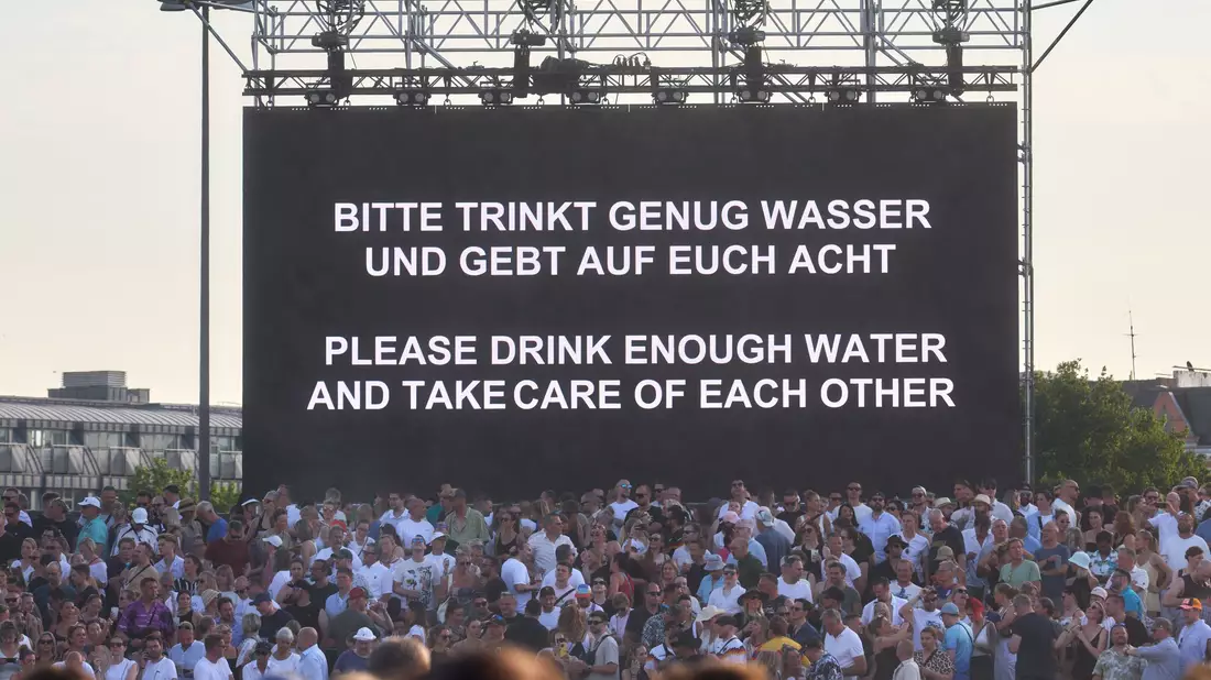 «Bitte trinkt genug Wasser und gebt auf Euch Acht» steht bei hochsommerlichen Temperaturen auf einer Leinwand bei einem Konzert von Techno-Star Paul Kalkbrenner auf dem Heiligengeistfeld in Hamburg. - Bild: Marcus Golejewski/dpa