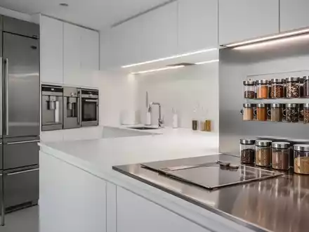 Eine moderne, minimalistische Küche mit Edelstahloberflächen, integrierten Geräten und magnetischen Gewürzdosen an einer Wand. - Foto: über boerse-global.de