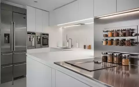 Eine moderne, minimalistische Küche mit Edelstahloberflächen, integrierten Geräten und magnetischen Gewürzdosen an einer Wand. - Foto: über boerse-global.de