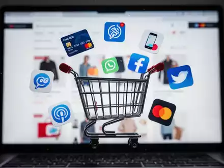 Ein stilisiertes Einkaufswagensymbol umgeben von digitalen Zahlungssymbolen vor einem verschwommenen Bildschirm einer E-Commerce-Website. - Foto: über boerse-global.de