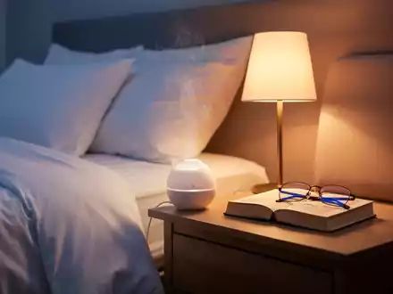 Ein ruhiges Schlafzimmer bei Dämmerung mit einem aufgeräumten Bett, sanftem Licht, einem Aromadiffusor und einem Buch auf dem Nachttisch. - Foto: über boerse-global.de