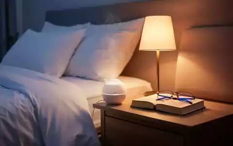 Ein ruhiges Schlafzimmer bei Dämmerung mit einem aufgeräumten Bett, sanftem Licht, einem Aromadiffusor und einem Buch auf dem Nachttisch. - Foto: über boerse-global.de