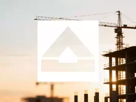 Abstrakte Baustelle bei Sonnenaufgang, mit Kranen und Gebäudestrukturen, die Wachstum und Stabilität im Bausektor andeuten. - Foto: über boerse-global.de