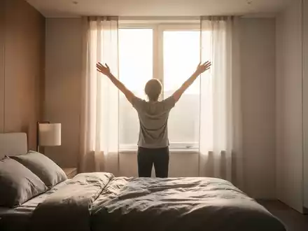 Eine Person streckt sich in einem modernen Schlafzimmer dem Morgenlicht entgegen, symbolisiert den Start in einen aktiven Tag. - Foto: über boerse-global.de