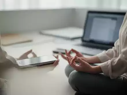 Eine Person meditiert ruhig in einem minimalistischen Büroumfeld, umgeben von weichem Licht, im Hintergrund verschwommene digitale Geräte. - Foto: über boerse-global.de
