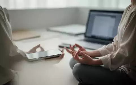 Eine Person meditiert ruhig in einem minimalistischen Büroumfeld, umgeben von weichem Licht, im Hintergrund verschwommene digitale Geräte. - Foto: über boerse-global.de