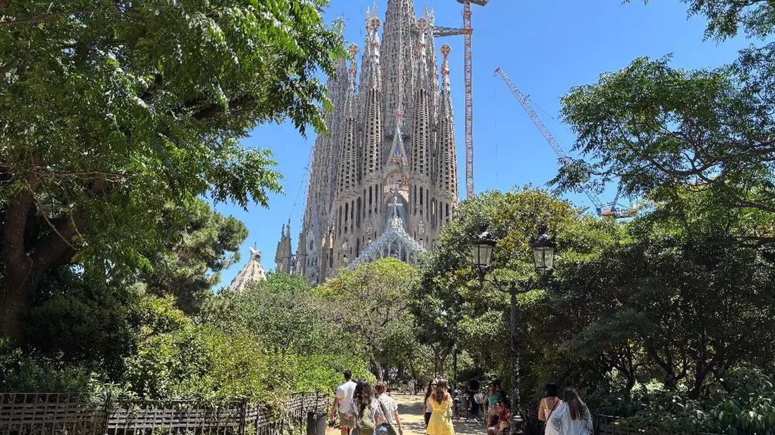 Touristen suchen bei großer Hitze den Schatten auf der Placa de la Sagrada Familia vor der gleichnamigen Basilika in Barcelona. (Archivbild) - Bild: Jan Uwe Ronneburger/dpa