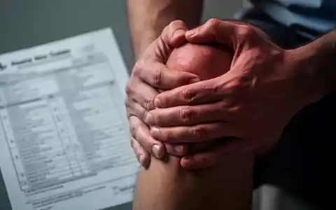 Eine Person hält sich schmerzverzerrt das Knie, im Hintergrund verschwommene medizinische Unterlagen. Symbolisiert Schmerz und Missachtung. - Foto: über boerse-global.de