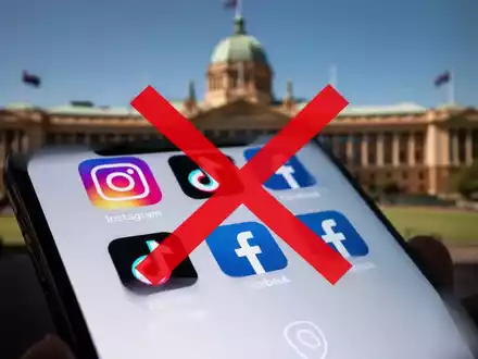 Ein Smartphone mit Social-Media-Icons und einem roten 'X', das ein Verbot symbolisiert, vor einem verschwommenen Regierungsgebäude. - Foto: über boerse-global.de