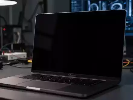Nahaufnahme eines modernen MacBook Pro mit schwarzem, nicht reagierendem Bildschirm in einem schwach beleuchteten, technischen Umfeld. - Foto: über boerse-global.de